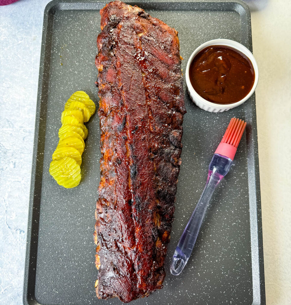 oven baked ribs on a sheet pan with BBQ sauce and pickles