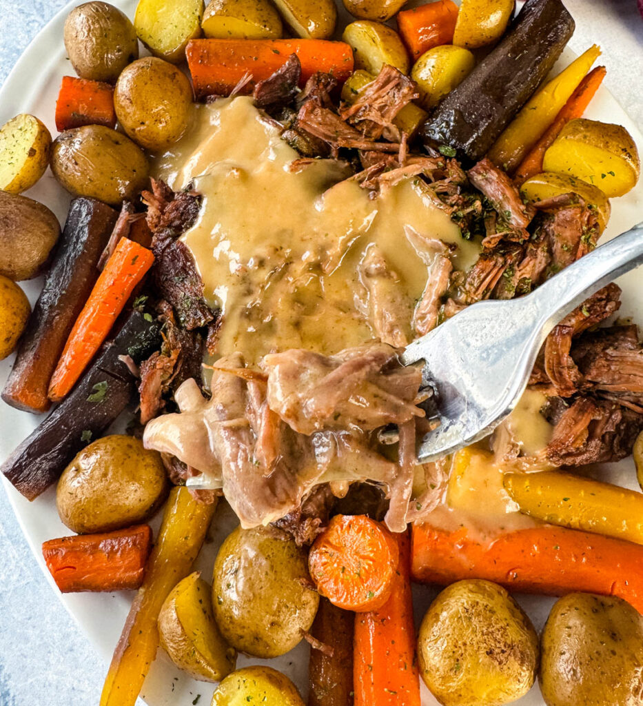 a forkful of cooked beef pot roast, carrots, and potatoes on a white plate