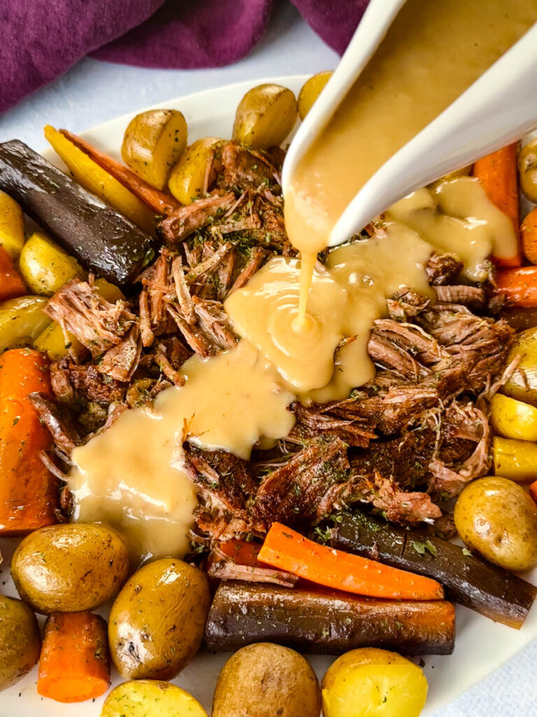 cooked beef pot roast, carrots, and potatoes drizzled with gravy on a white plate