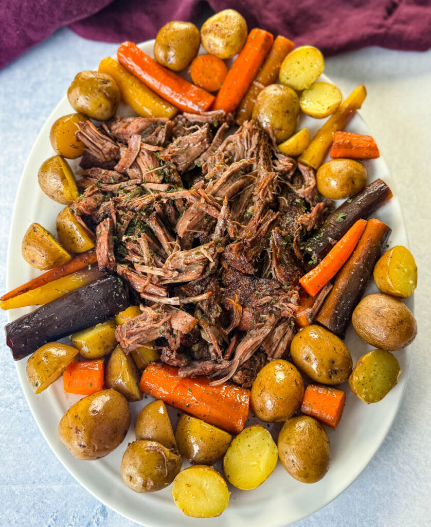 cooked beef pot roast, carrots, and potatoes on a white plate