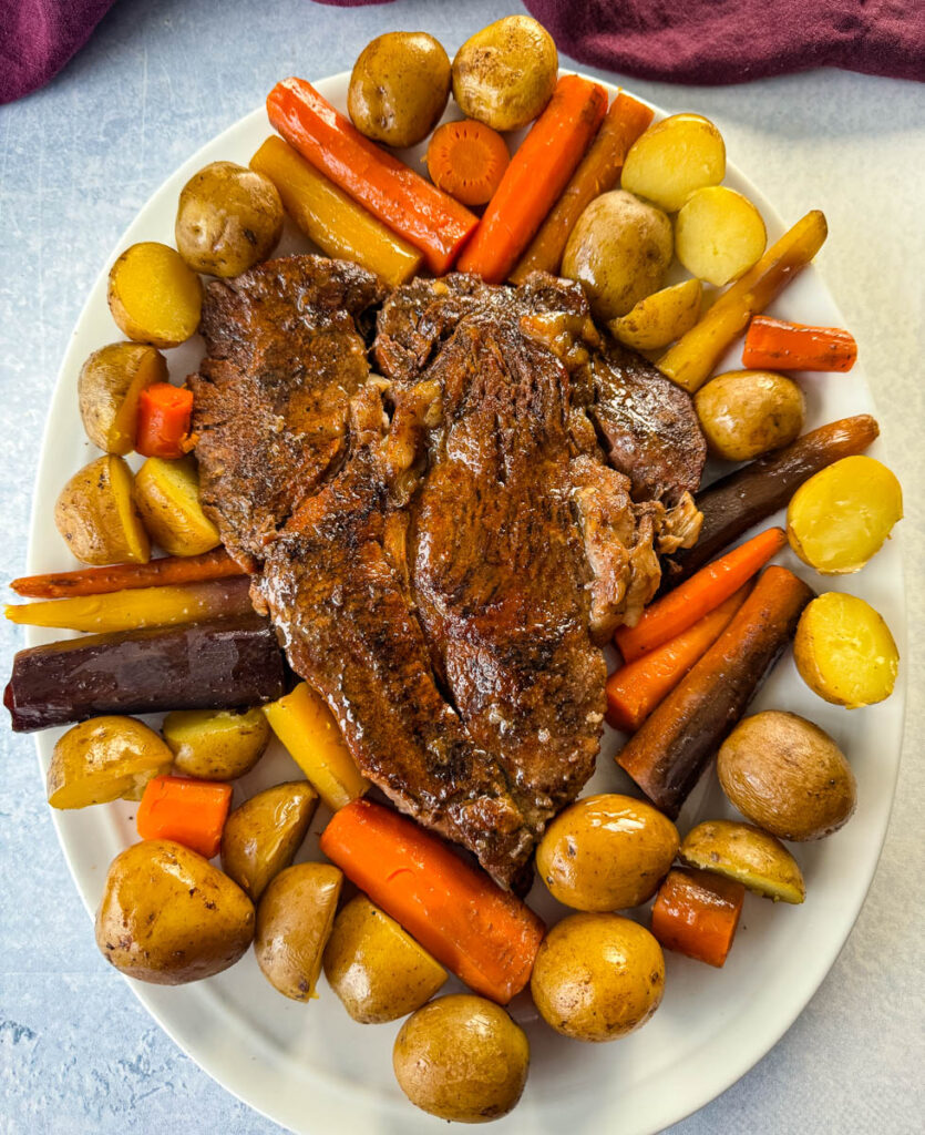 cooked beef pot roast, carrots, and potatoes on a white plate