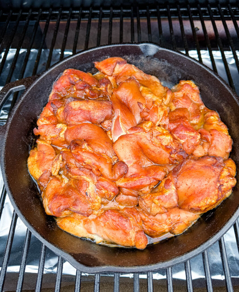 raw chicken thighs in a cast iron skillet on a Traeger pellet grill smoker
