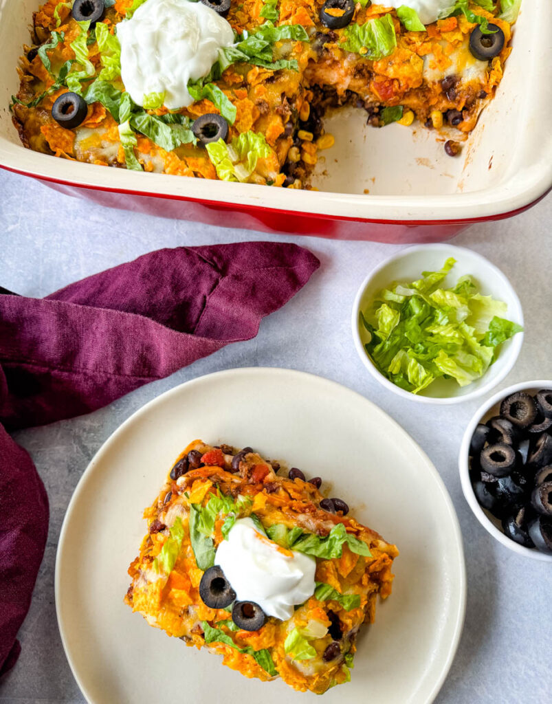 taco bake caserole on a plate with Doritos, olives, lettuce, and sour cream