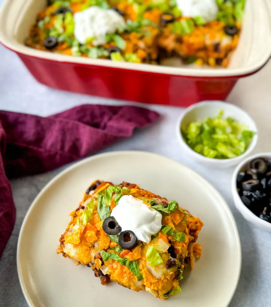 taco bake caserole on a plate with Doritos, olives, lettuce, and sour cream