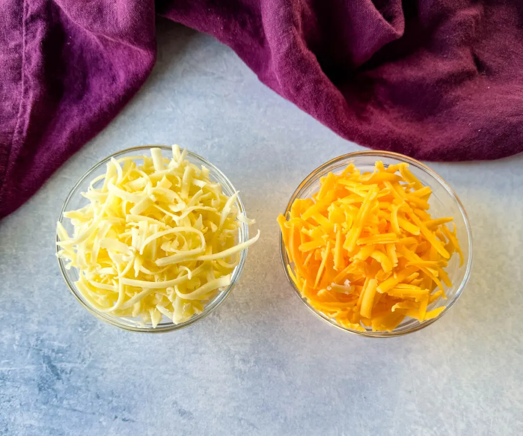 grated cheddar and monterey jack cheese in separate glass bowls