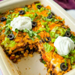 taco bake caserole in a baking dish with Doritos, olives, lettuce, and sour cream
