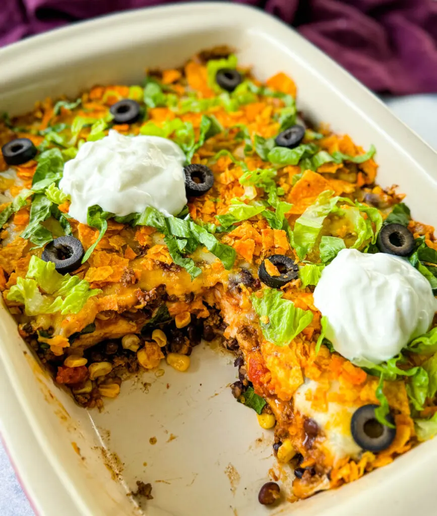 taco bake caserole in a baking dish with Doritos, olives, lettuce, and sour cream