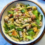 Chicken Caesar Pasta Salad with bacon and croutons in a white bowl