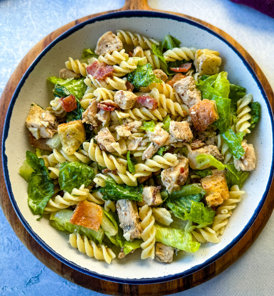 Chicken Caesar Pasta Salad with bacon and croutons in a white bowl
