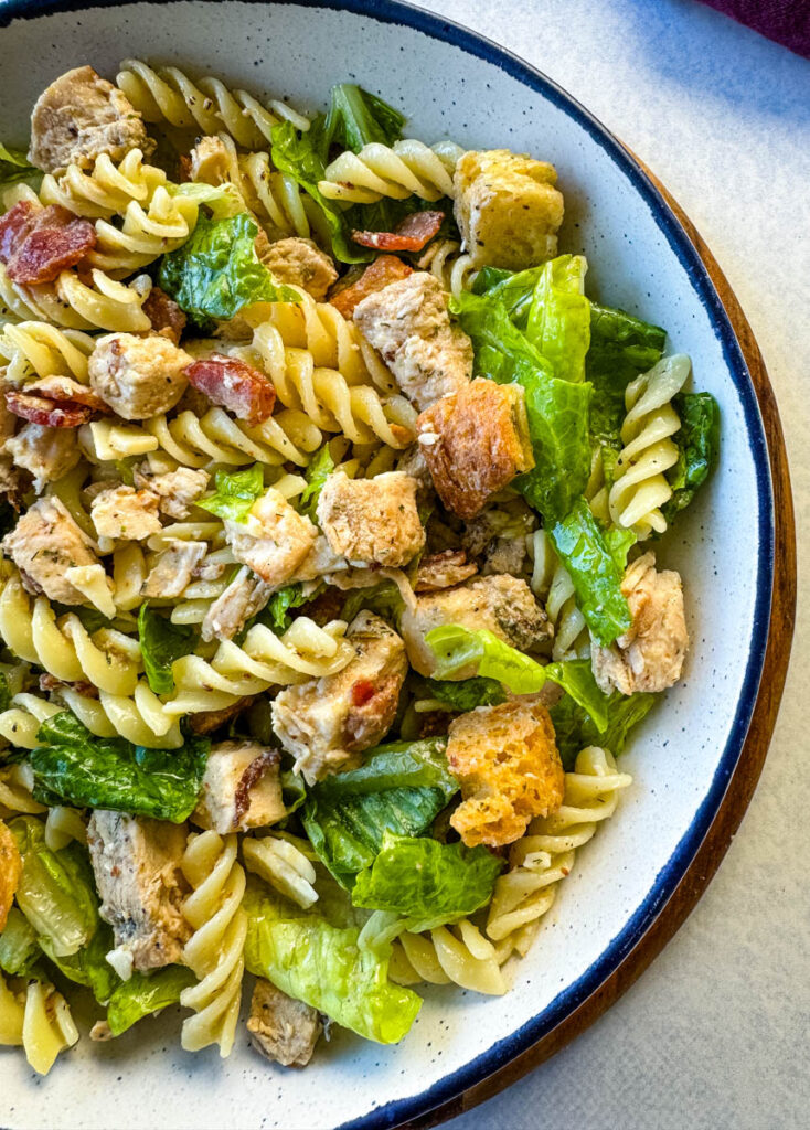 Chicken Caesar Pasta Salad with bacon and croutons in a white bowl