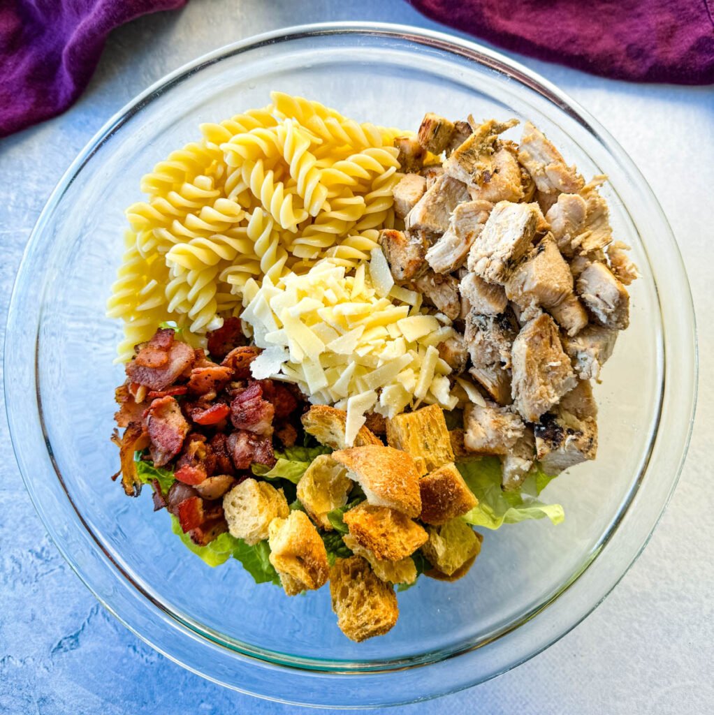 Chicken Caesar Pasta Salad with bacon and croutons in a glass bowl