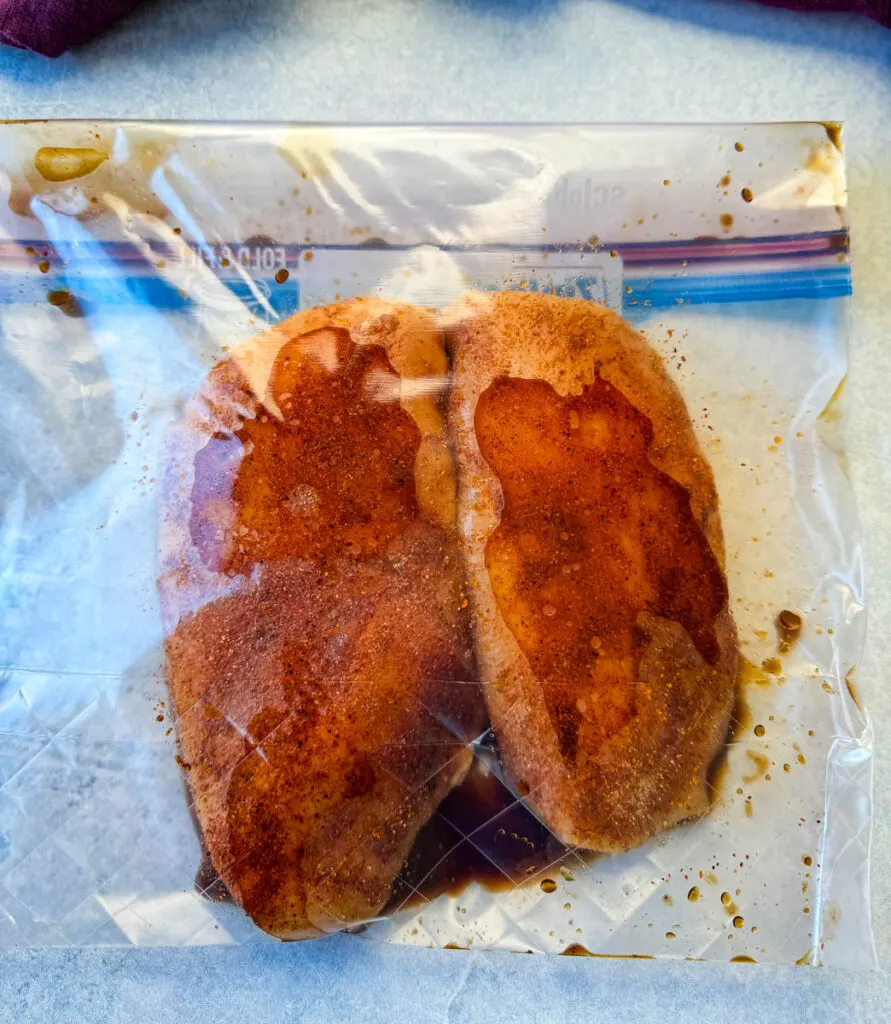 2 chicken breasts marinated with spices in a plastic bag