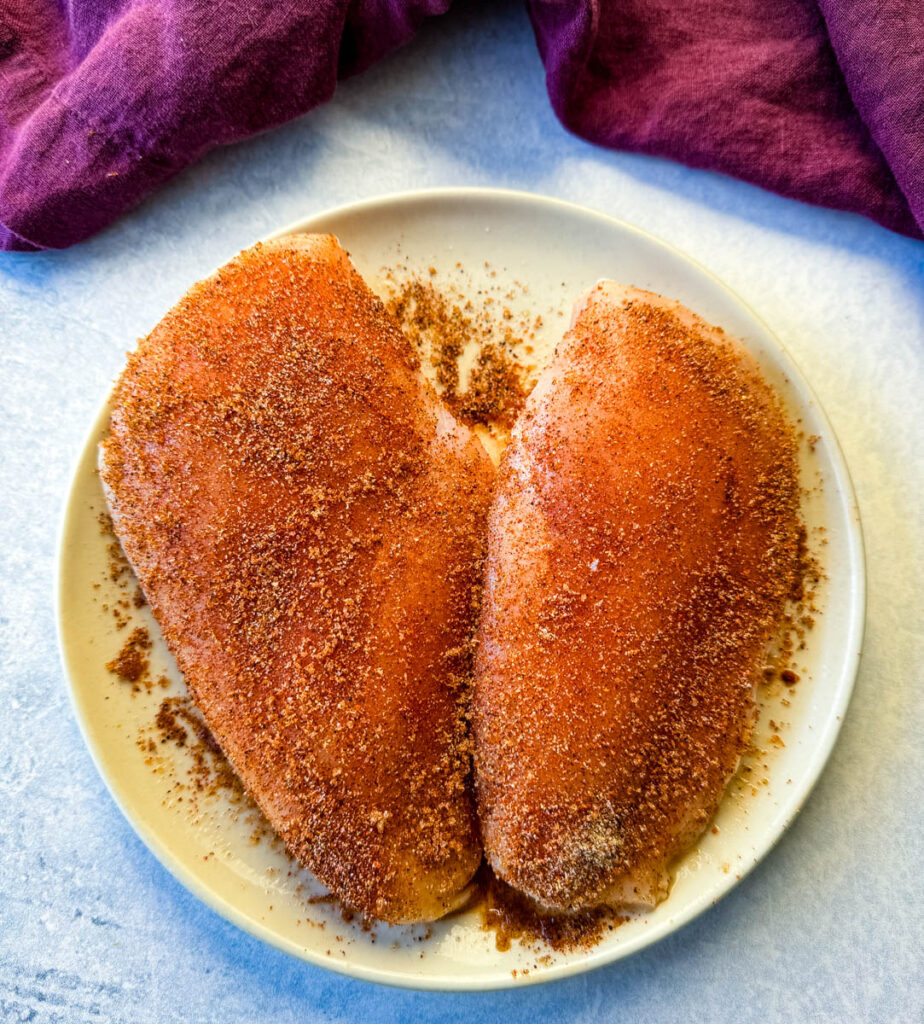 2 seasoned raw chicken breasts on a plate