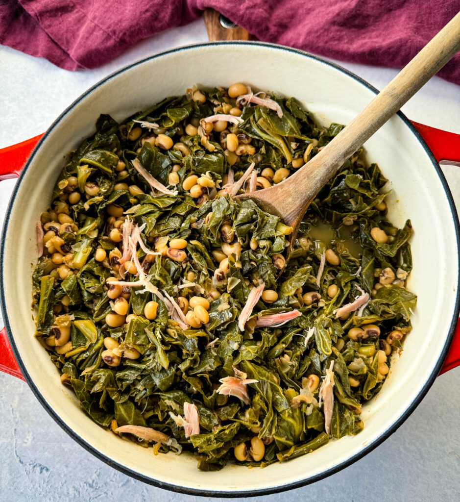 collard greens and black eyed peas with smoked turkey in a red Dutch oven with a wooden spoon