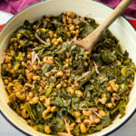 collard greens and black eyed peas with smoked turkey in a red Dutch oven with a wooden spoon