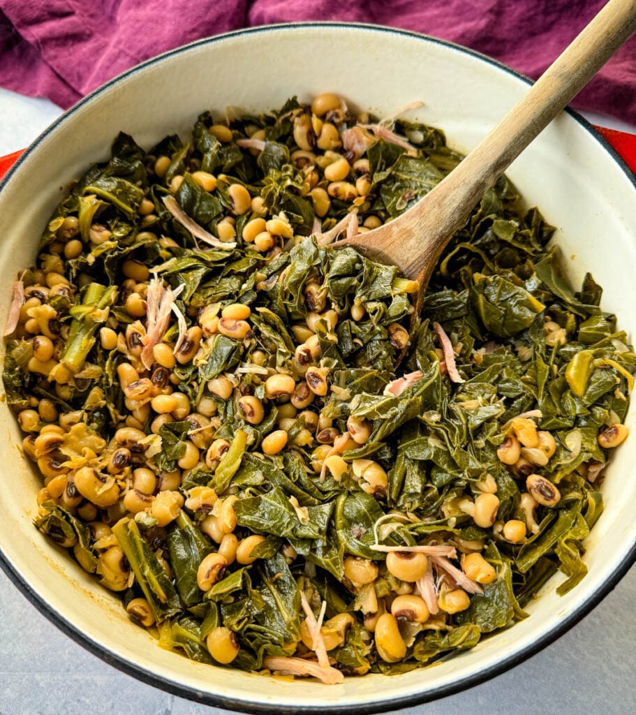 collard greens and black eyed peas with smoked turkey in a red Dutch oven with a wooden spoon