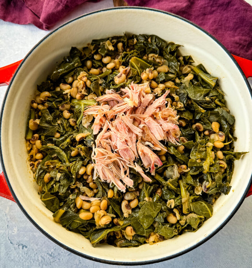 collard greens and black eyed peas with smoked turkey in a red Dutch oven with a wooden spoon