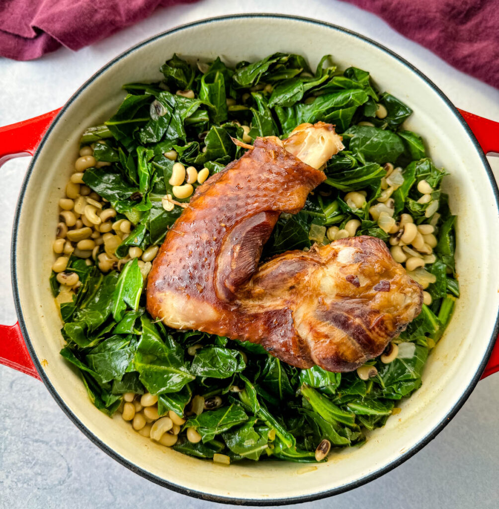 collard greens and black eyed peas with smoked turkey in a red Dutch oven with a wooden spoon