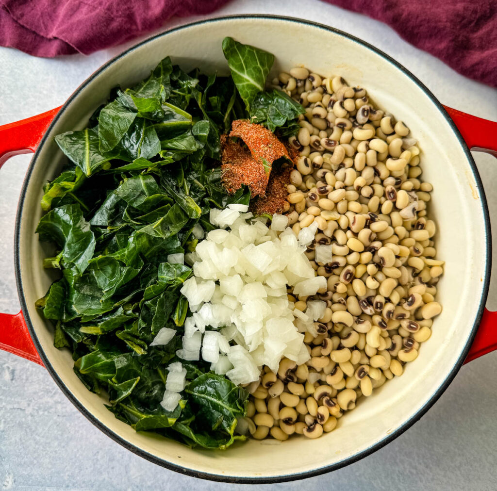 uncooked collard greens and black eyed peas in a red Dutch oven