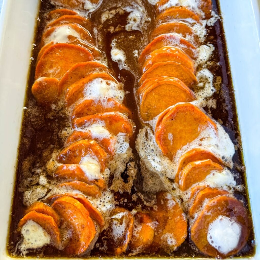 candied sweet potatoes with marshmallows in a baking dish drizzled with glaze in a wooden spoon