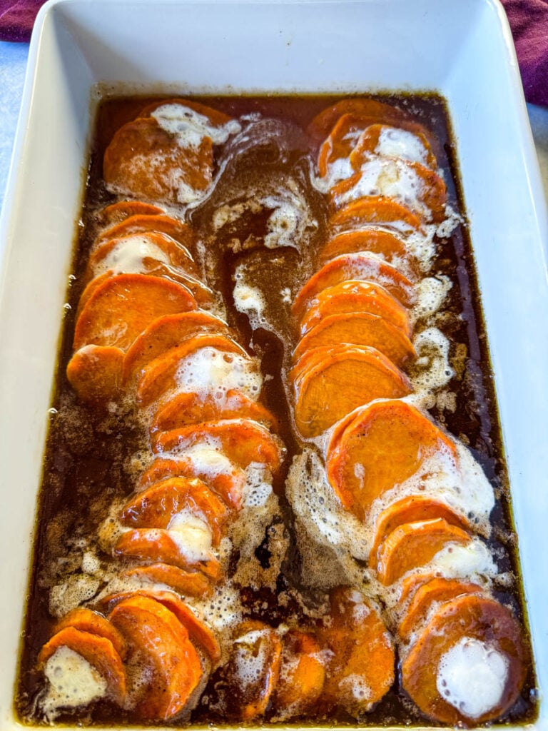 candied sweet potatoes with marshmallows in a baking dish drizzled with glaze in a wooden spoon