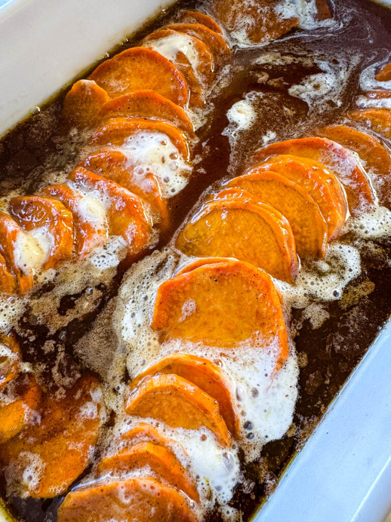 candied sweet potatoes with marshmallows in a baking dish drizzled with glaze in a wooden spoon