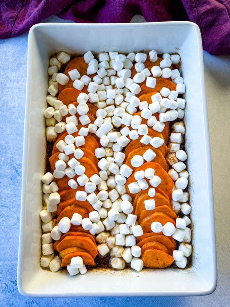 sliced sweet potatoes with marshmallows and brown sugar cinnamon glaze in a white baking dish