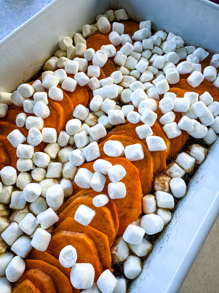 sliced sweet potatoes with marshmallows and brown sugar cinnamon glaze in a white baking dish