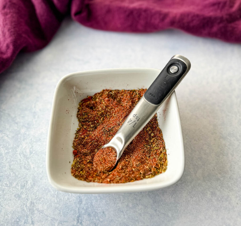 collard greens seasoning dry spices in a white bowl with a measuring spoon