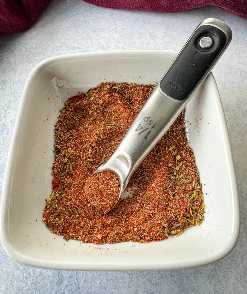 collard greens seasoning dry spices in a white bowl with a measuring spoon
