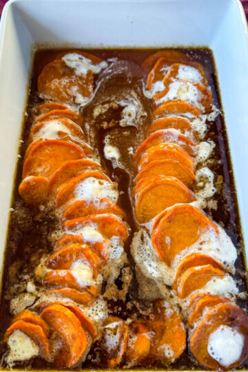candied sweet potatoes with marshmallows in a baking dish drizzled with glaze in a wooden spoon