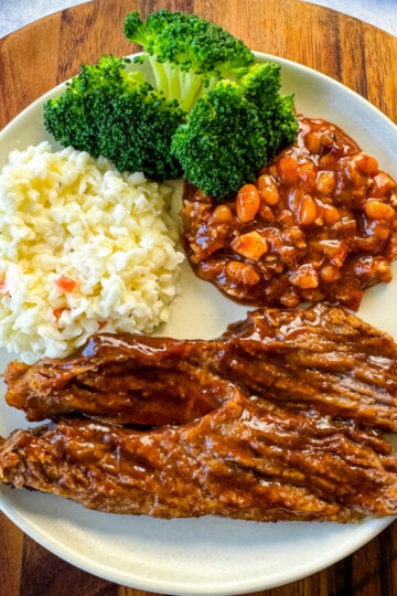 slow cooker Crockpot beef brisket with BBQ sauce on a plate with beans, broccoli, and coleslaw