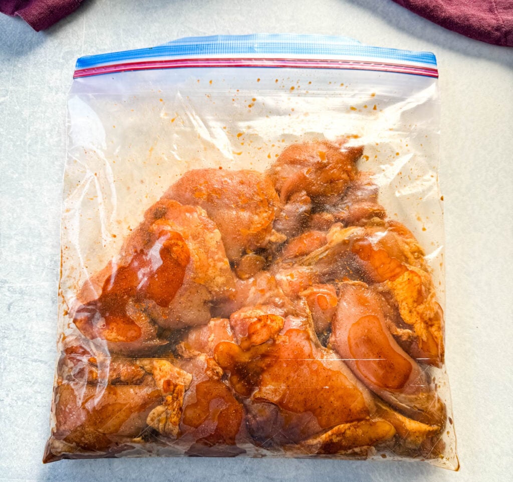 raw chicken thighs drizzled in homemade grilled chicken seasoning marinade in a plastic bag