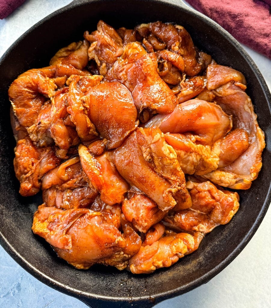 raw chicken thighs drizzled in homemade grilled chicken seasoning marinade in a cast iron skillet