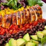 grilled chicken on a plate with vegetables and avocado