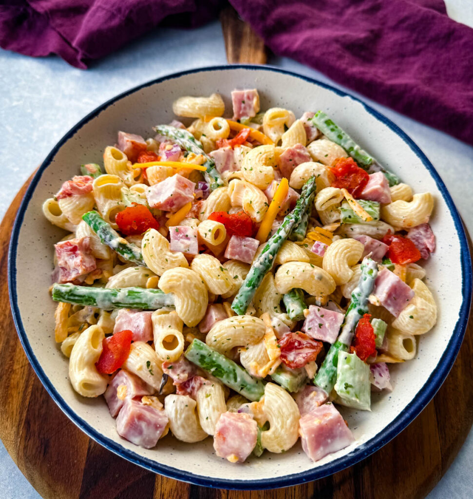 ham pasta salad with cheese, asparagus and tomatoes in a white bowl