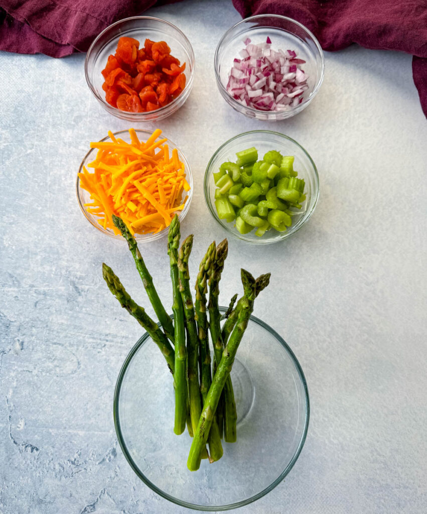 chopped tomatoes, onions, grated cheese, diced celery, and asparagus in separate glass bowls