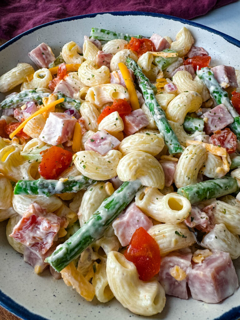 ham pasta salad with cheese, asparagus and tomatoes in a white bowl