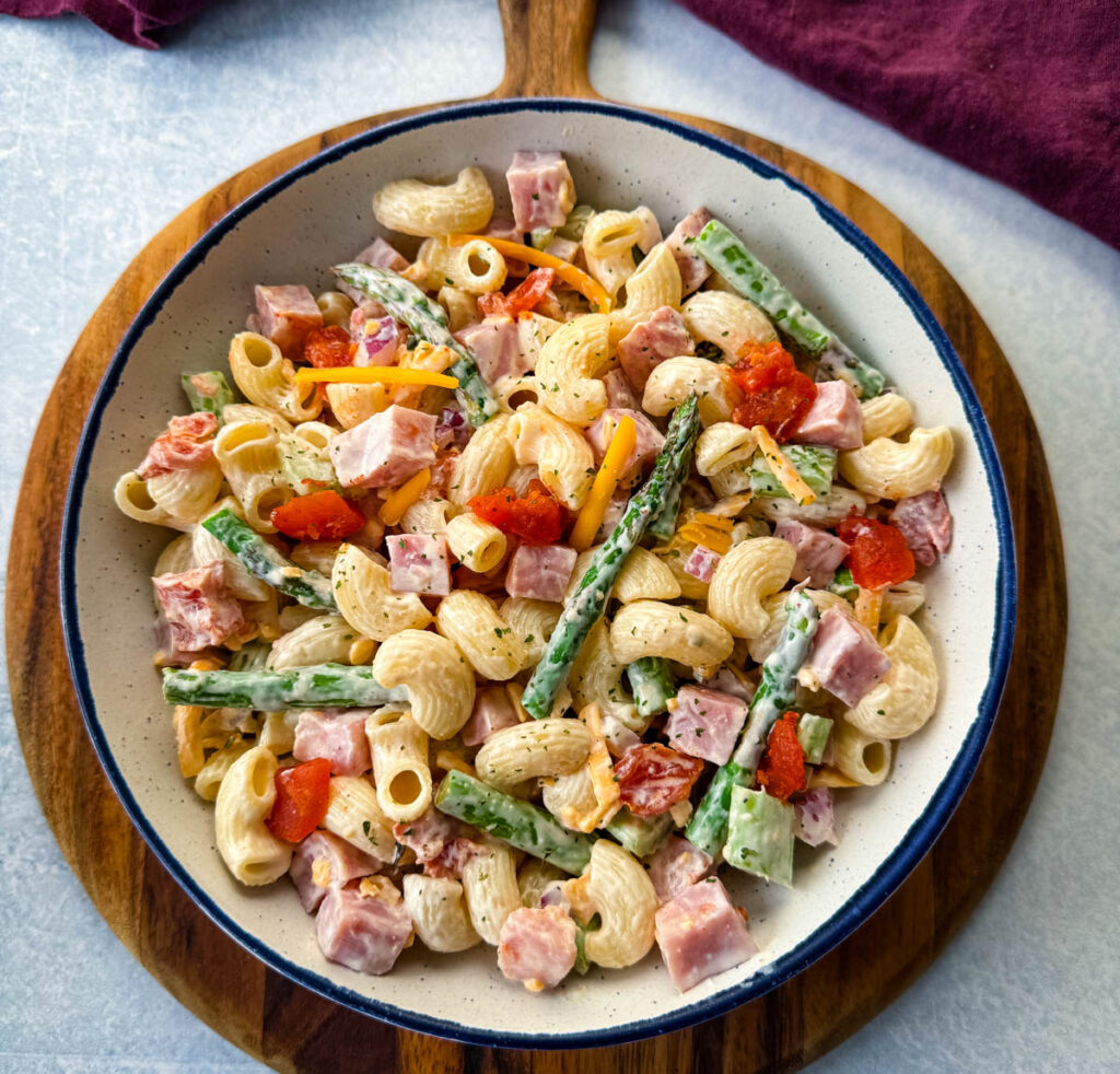 ham pasta salad with cheese, asparagus and tomatoes in a white bowl