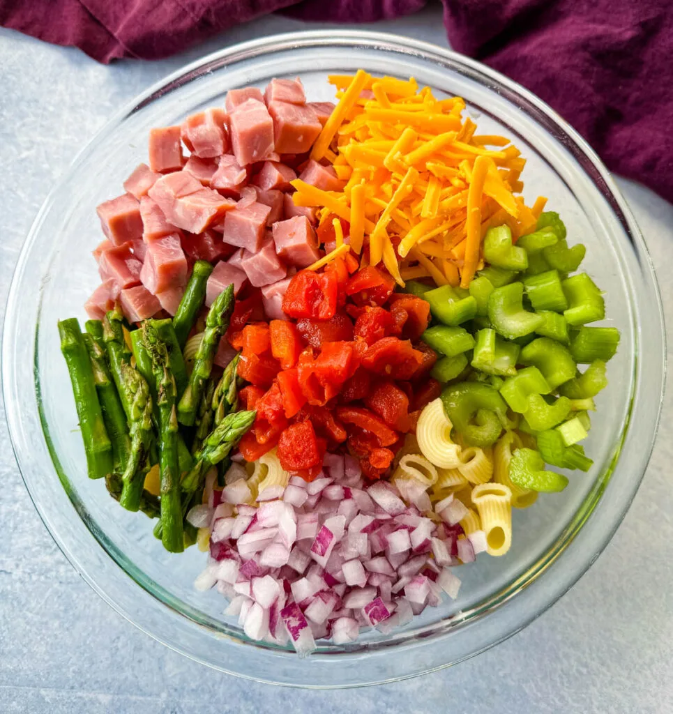 ham pasta salad with cheese, asparagus and tomatoes in a glass bowl