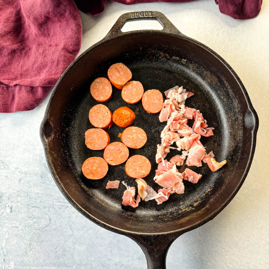 uncooked sausage and bacon in a cast iron skillet