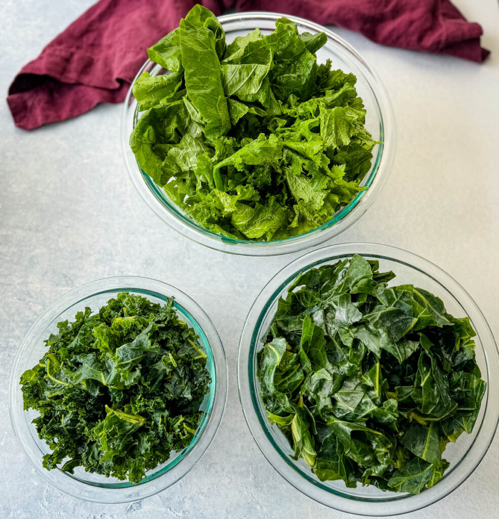 fresh collard greens, kale, turnip greens, and mustard greens in separate glass bowls