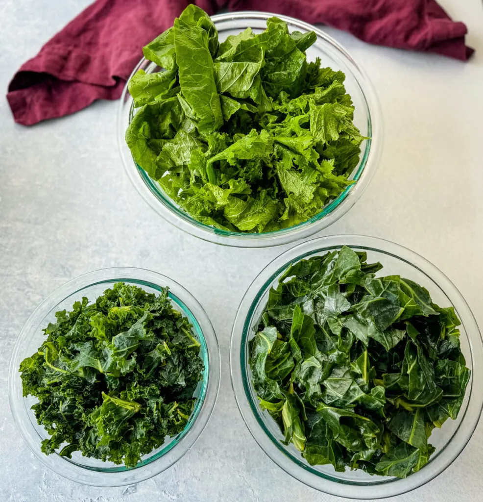 fresh collard greens, kale, turnip greens, and mustard greens in separate glass bowls