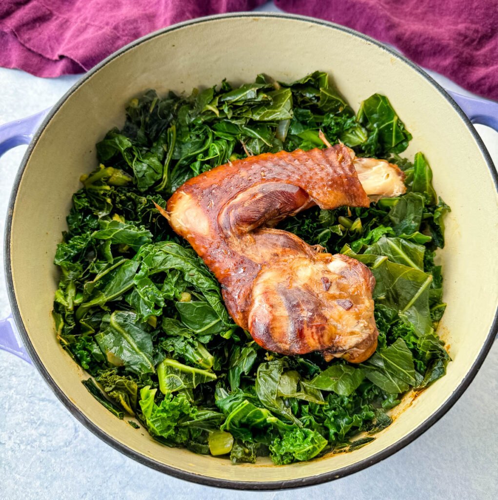 uncooked mixed greens in a Dutch oven with smoked turkey