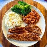 slow cooker Crockpot beef brisket with BBQ sauce on a plate with beans, broccoli, and coleslaw