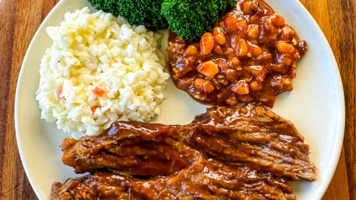 slow cooker Crockpot beef brisket with BBQ sauce on a plate with beans, broccoli, and coleslaw