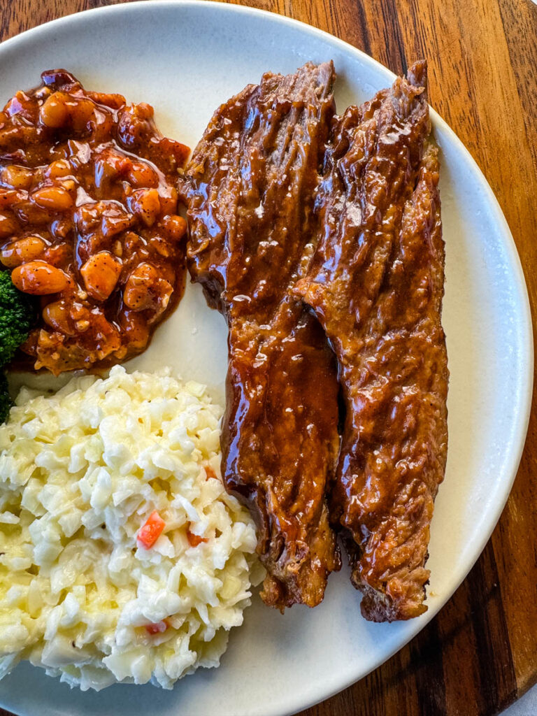 slow cooker Crockpot beef brisket with BBQ sauce on a plate with beans and coleslaw