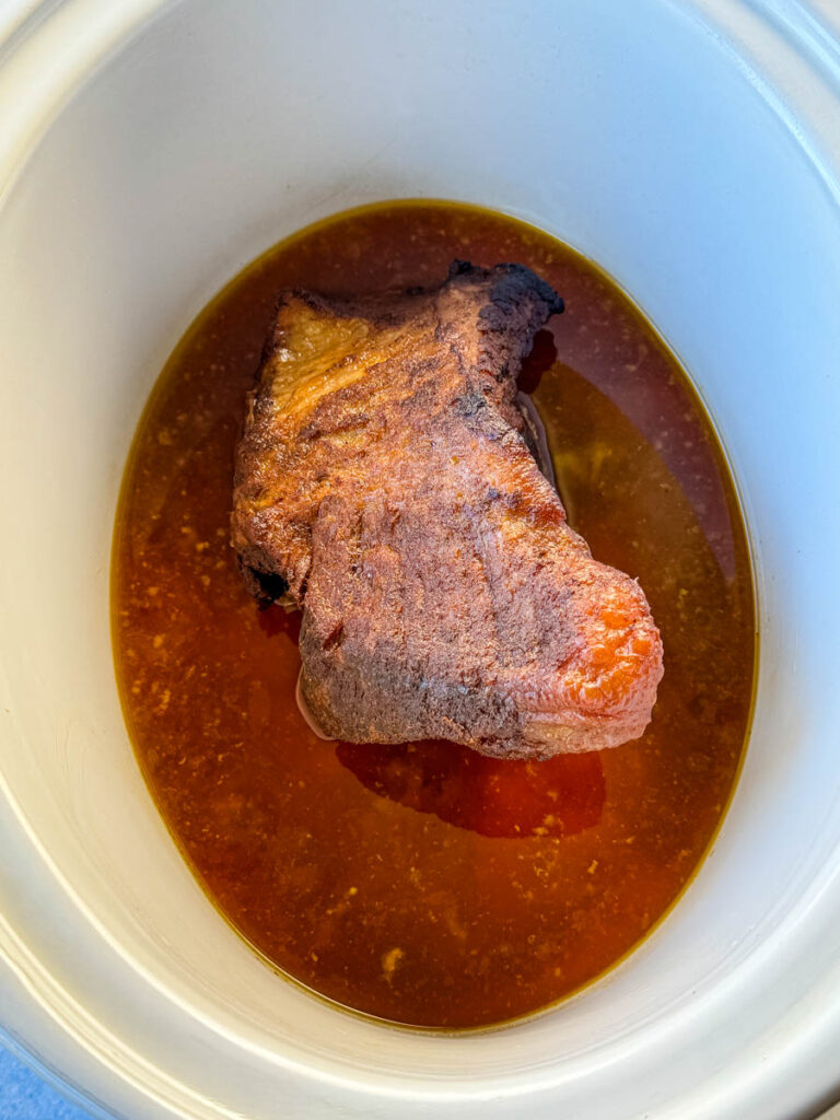 brisket in a white Crockpot slow cooker with broth