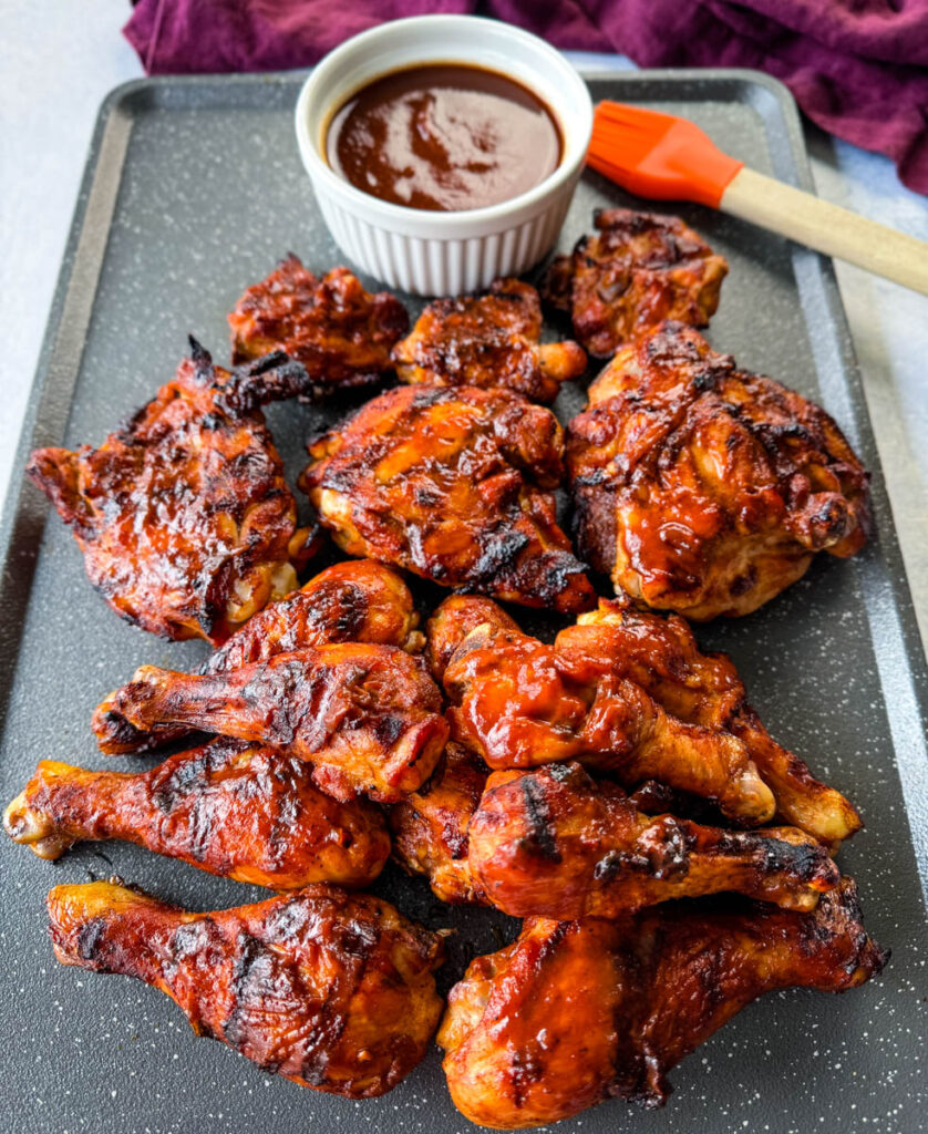 grilled bbq chicken thighs and drumsticks on a sheet pan with bbq sauce