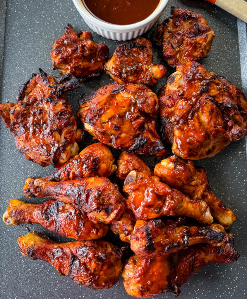 grilled bbq chicken thighs and drumsticks on a sheet pan with bbq sauce